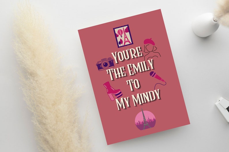 May include: A greeting card with a mauve background features the text "You're the Emily to my Mindy" with illustrations of a camera, high-heeled shoe, microphone, and Eiffel Tower. A stamp-like image of the Eiffel Tower is at the top.
