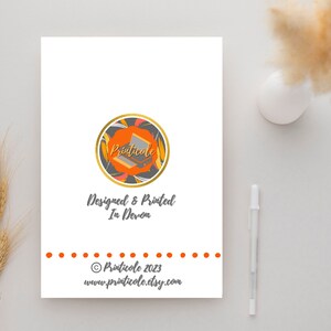 May include: A white card with a logo and text. The logo is a circle with orange, gold, and gray elements. Text includes "Designed & Printed In Devon" and the website address. A pen and decorative plant are in the background.