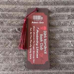 May include: A brown bookmark with a red tassel. The bookmark has a dark red background with white text that reads "Dark Romance Book Club Membership: Lifetime" and "Where: Wherever The Trigger Warnings Are For All The Morally Grey Girls".