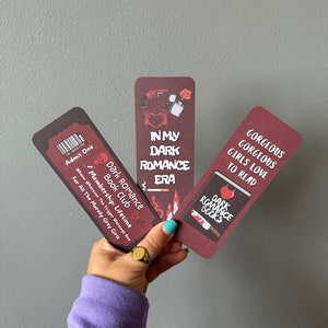 May include: Three bookmarks with a dark romance theme. The bookmarks are red with black text and illustrations. The text on the bookmarks reads "In My Dark Romance Era", "Dark Romance Books", and "Gorgeous Gorgeous Girls Love To Read".