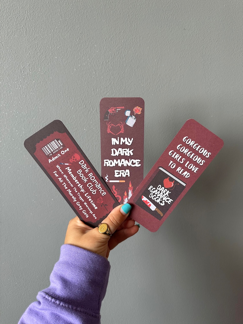 May include: Three bookmarks with a dark romance theme. The bookmarks are red with black text and illustrations. The text on the bookmarks reads "In My Dark Romance Era", "Dark Romance Books", and "Gorgeous Gorgeous Girls Love To Read".