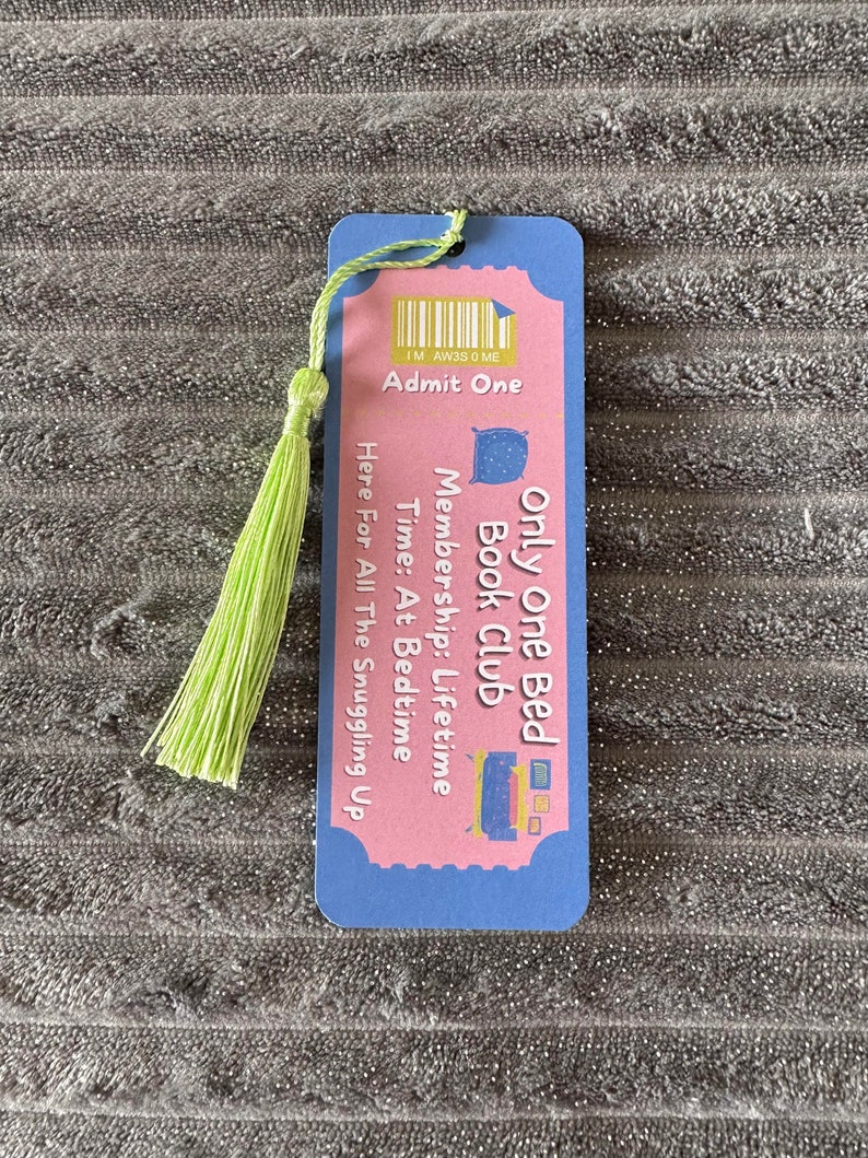 May include: A pink and blue bookmark with a green tassel. The bookmark has a ticket design with the text "Only One Bed Book Club" and "Membership: Lifetime".
