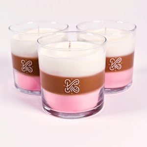 K&ouml;nnte beinhalten: Drei mehrschichtige Kerzen in transparenten Glasbeh&auml;ltern. Die Schichten sind rosa, braun und wei&szlig;. Jede Kerze hat einen wei&szlig;en Docht und ein wei&szlig;es Logo. Wohndekoration.