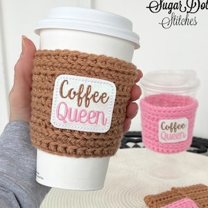 May include: A brown crocheted coffee cup sleeve with a white and pink "Coffee Queen" patch. A smaller pink crocheted cup sleeve and additional brown and pink sleeves are also visible.