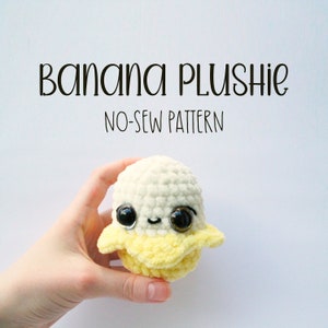 May include: A crocheted banana plush toy with a white body, yellow peel, and black eyes. The toy is being held in a hand. The text "Banana Plushie No-Sew Pattern" is above the toy.