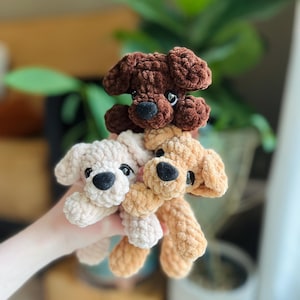 以下が含まれることがあります： 柔らかい質感の糸で作られた3匹の小さな犬のぬいぐるみ。1匹はダークブラウン、1匹はライトベージュ、もう1匹はタンカラーです。それぞれ垂れ耳、丸い黒い鼻、小さな黒いプラスチック製の目をしており、統一感のあるセットになっています。