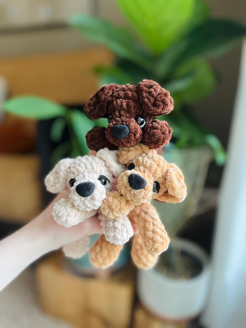 以下が含まれることがあります： 柔らかい質感の糸で作られた3匹の小さな犬のぬいぐるみ。1匹はダークブラウン、1匹はライトベージュ、もう1匹はタンカラーです。それぞれ垂れ耳、丸い黒い鼻、小さな黒いプラスチック製の目をしており、統一感のあるセットになっています。