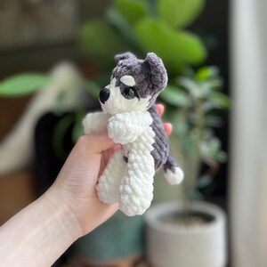 May include: A handmade crochet puppy toy in shades of gray and white. The plush dog has a black nose, black eyes, and floppy ears. The toy is approximately 5 inches tall and has a soft, textured appearance.