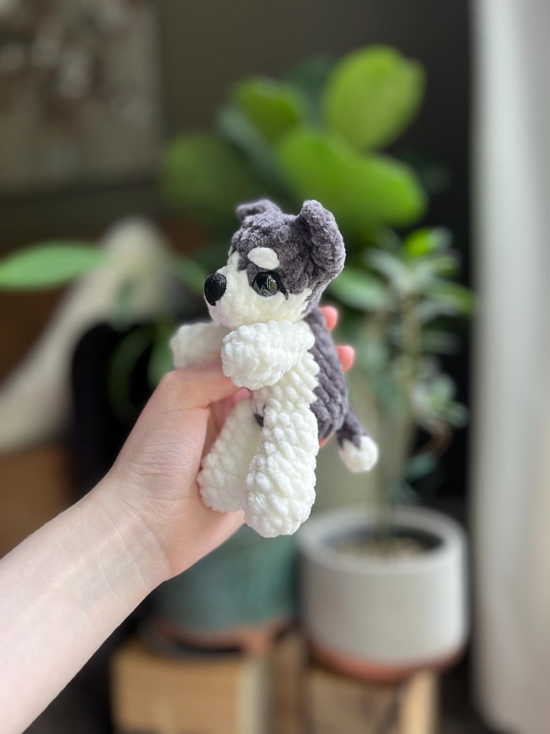 May include: A handmade crochet puppy toy in shades of gray and white. The plush dog has a black nose, black eyes, and floppy ears. The toy is approximately 5 inches tall and has a soft, textured appearance.