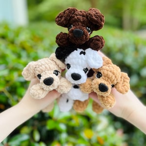 以下が含まれることがあります： 柔らかい質感の糸で編まれた、4匹の小さな犬のぬいぐるみ。ダークブラウン、ライトベージュ、黒いアクセントのある白、タンカラーの犬たちで、それぞれ黒いプラスチックの目と黒い刺繍の鼻が特徴です。