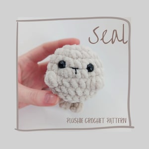 May include: A crocheted plush seal in a light beige color. The seal has black eyes and a small black line for a mouth. The word "Seal" is written in a handwritten font. The text "PLUSHIE CROCHET PATTERN" is written below the seal.