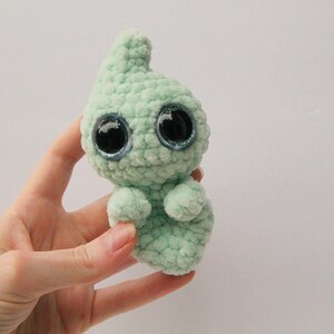 Puede incluir: Un juguete de peluche fantasma verde tejido a crochet con grandes ojos brillantes.