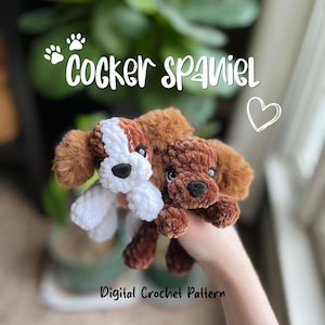 Op de afbeelding: Twee gehaakte Cocker Spaniel hondenknuffels, één bruin en wit, de andere effen bruin, worden omhoog gehouden tegen een vage groene achtergrond. De tekst "Cocker Spaniel" staat boven de honden en "Digital Crochet Pattern" staat eronder.