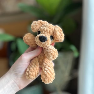 以下が含まれることがあります： 柔らかく質感のあるシェニール糸で作られた、小さなライトブラウンの犬のぬいぐるみ。垂れ耳、黒い鼻を持つ丸みを帯びた鼻先、暗く光沢のある目が特徴です。手足は短く丸みを帯びており、コンパクトな外観をしています。