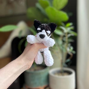 May include: A handmade crochet dog toy in black and white. The dog has black ears, a black nose, and white eyes. The dog's body and legs are white. The toy is soft and plush.