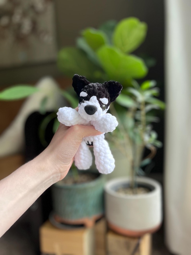 May include: A handmade crochet dog toy in black and white. The dog has black ears, a black nose, and white eyes. The dog's body and legs are white. The toy is soft and plush.