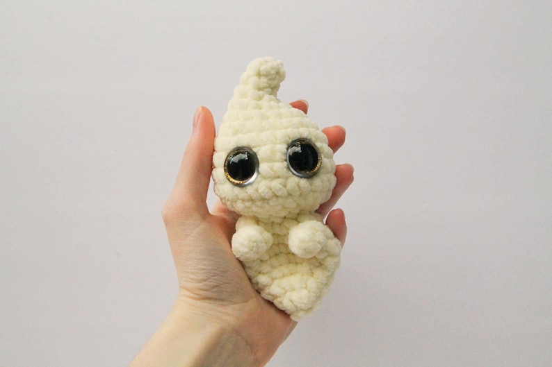 Puede incluir: Un juguete de peluche de fantasma tejido a crochet con grandes ojos saltones. El fantasma es blanco y tiene una forma redondeada.