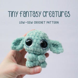 Könnte beinhalten: Eine gehäkelte grüne Kreatur mit großen schwarzen Augen. Die Kreatur hat zwei schlaffe Ohren und sitzt in einer Hand. Der Text "Tiny fantasy creatures" und "Low-sew crochet pattern" befindet sich über der Kreatur.