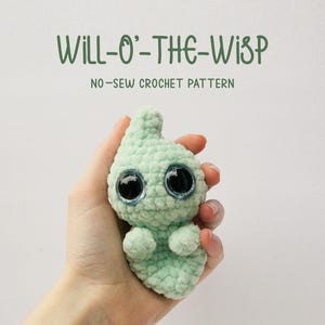 May include: A crocheted green ghost with large black eyes. The ghost is being held in a hand. The text "WILL-O'-THE-WISP NO-SEW CROCHET PATTERN" is above the ghost.