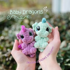 May include: Two handmade crochet baby dragons in a person's hands. One dragon is purple with pink accents, the other is mint green with blue accents. The text "Baby Dragons" and "Plushie crochet pattern" are in the image.