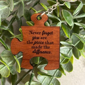 May include: Wooden puzzle piece keychain with the text "Never forget you are the piece that made the difference."
