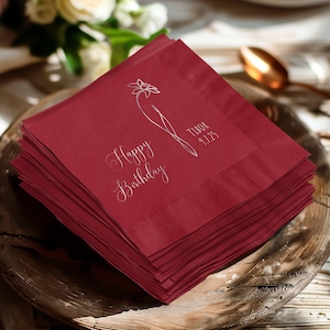 Könnte beinhalten: Ein Stapel weinroter Papierservietten mit einem silbernen Blumendesign und dem Schriftzug "Happy Birthday". Die Servietten enthalten auch den Namen "Tibor" und das Datum "9.7.25".