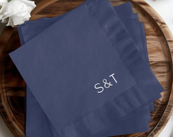 May include: Stack of navy blue paper napkins with the initials "S&T" embroidered in silver on the top napkin.