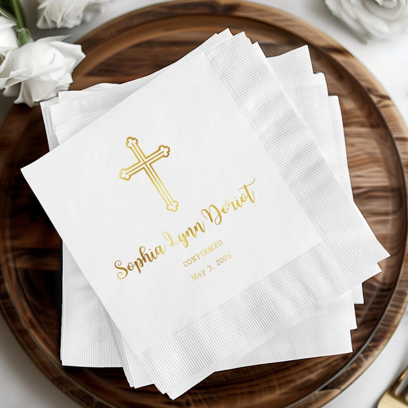 May include: White paper napkins with a gold cross design and custom text. The napkins are stacked on a wooden tray. The text reads "Sophia Lynn Doriot Confirmed May 3, 2026".