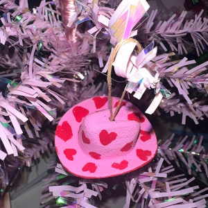 May include: Pink cowboy hat Christmas ornament with red heart designs.