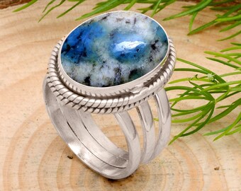 May include: A silver ring featuring an oval blue and white stone. The stone is set in a silver bezel with a rope design. The ring has a split shank design with three parallel bands. The ring is a piece of jewellery.