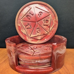 May include: Set of six red and gold resin coasters with a dice design. Each coaster features a different number from 1 to 6. The coasters are in a holder with a swirl design.