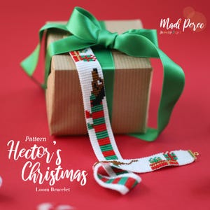 Può includere: Un braccialetto a telaio a tema natalizio, con un disegno di una persona in abito rosso e verde. Il braccialetto è bianco con strisce rosse e verdi ed è esposto con un regalo confezionato e un nastro verde. Il testo "Hector's Christmas" è visibile.