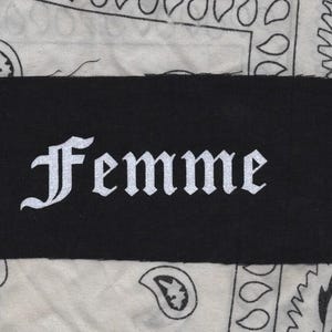 May include: A black fabric patch with the word "Femme" written in white, stylized lettering.