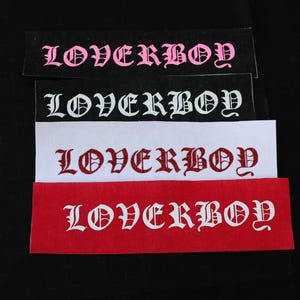 May include: Four fabric patches with the word "LOVERBOY" written in different colors and fonts. The patches are black, white, red, and pink.