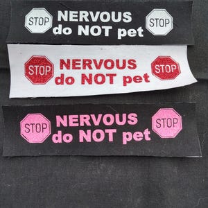 May include: Three black and white fabric patches with red and pink "STOP" signs and the text "NERVOUS do NOT pet".