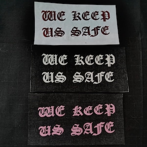 May include: Three versions of a sticker with the text "WE KEEP US SAFE" in a gothic font. The first sticker is on white paper with red lettering. The second sticker is on black paper with white lettering. The third sticker is on black paper with pink lettering.