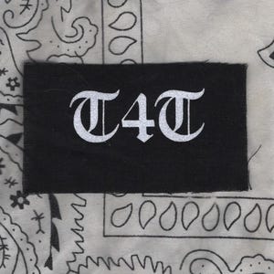 May include: Black patch with white lettering that reads "T4T" in a gothic font.