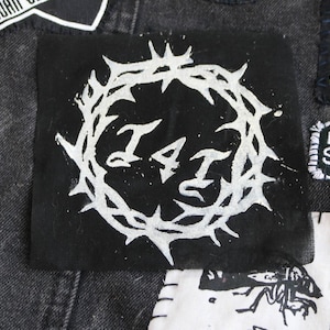 May include: A black and white patch with a thorned circle around the letters "I4I".