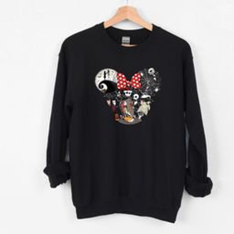 May include: Black crew neck sweatshirt with a graphic of a Mickey Mouse head filled with characters and scenes from "The Nightmare Before Christmas." The design includes Jack Skellington, Sally, and a red polka dot bow. The sweatshirt has long sleeves and a ribbed collar.