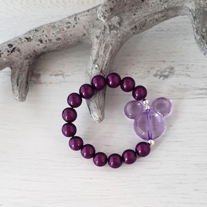 May include: A purple beaded bracelet with a purple Mickey Mouse charm. The bracelet is made with small, round beads and is strung on a silver chain.