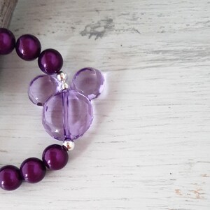 May include: Purple beaded bracelet with a clear purple Mickey Mouse charm.