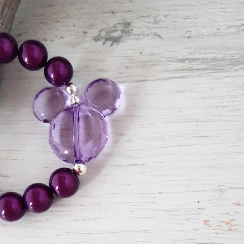 May include: Purple beaded bracelet with a clear purple Mickey Mouse charm.