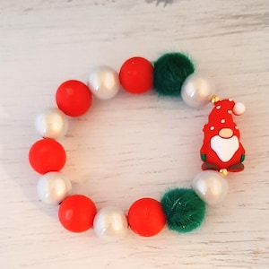 May include: A Christmas-themed bracelet with red, white, and green beads, and a red gnome charm. The bracelet includes round beads and fluffy green accents. A cheerful accessory for the festive season.