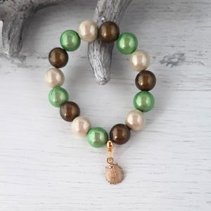 Könnte beinhalten: Ein Armband aus grünen, braunen und cremefarbenen Perlen mit einem goldenen Muschel-Anhänger.