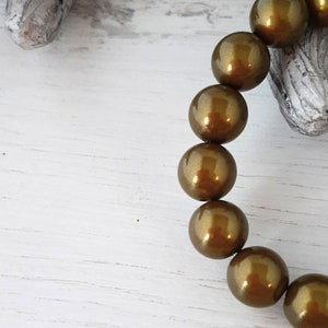 May include: A strand of round, gold-colored beads with a shiny, metallic finish. The beads are strung together on a clear thread.