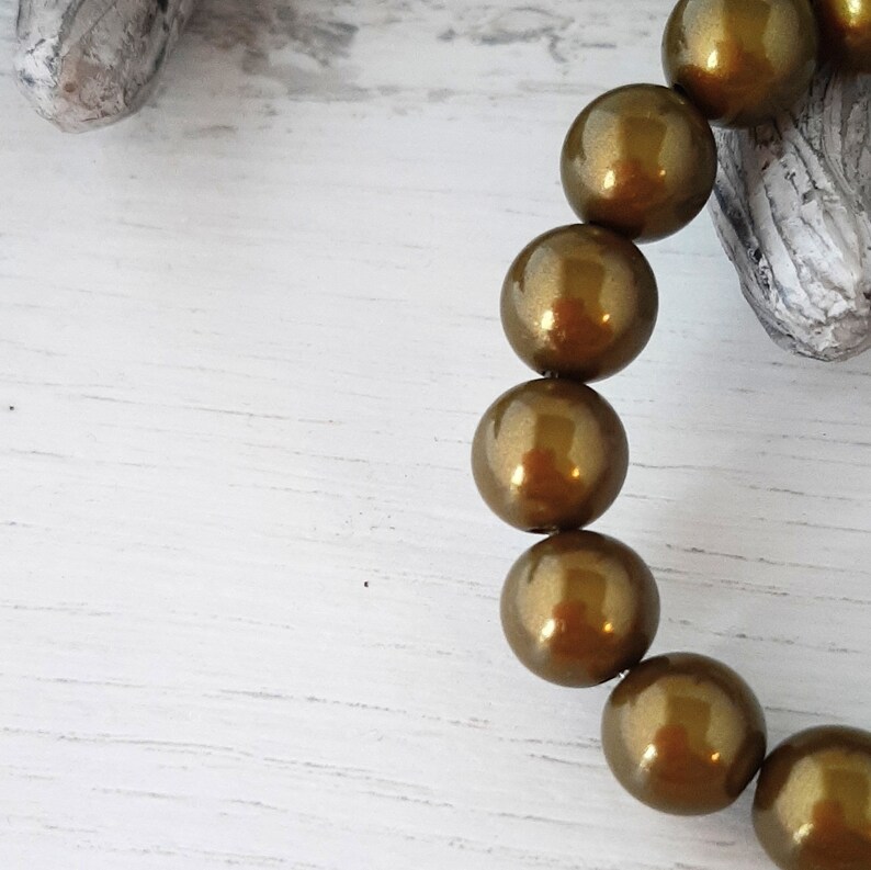 May include: A strand of round, gold-colored beads with a shiny, metallic finish. The beads are strung together on a clear thread.