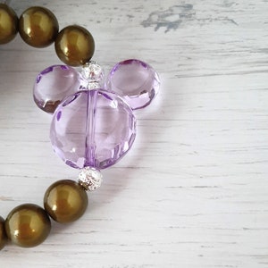 May include: A purple glass Mickey Mouse charm with silver beads on a brown beaded bracelet.