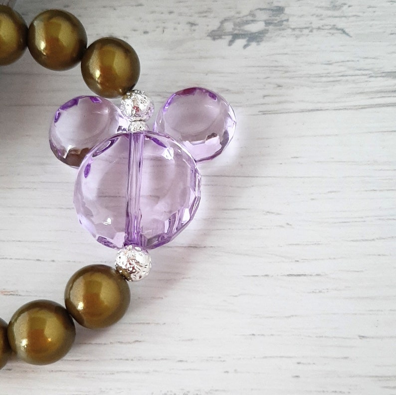 May include: A purple glass Mickey Mouse charm with silver beads on a brown beaded bracelet.