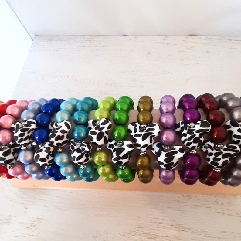 May include: A set of 12 colorful bracelets with a black and white cow print bow. Each bracelet is made of large, round, shiny beads.