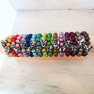 May include: A set of 16 colorful bracelets with a cow print design. Each bracelet is made of round beads and has a different color.